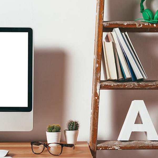 Computer, glasses, potted plants on desk; bookshelf with books, headphones, and large letter A.