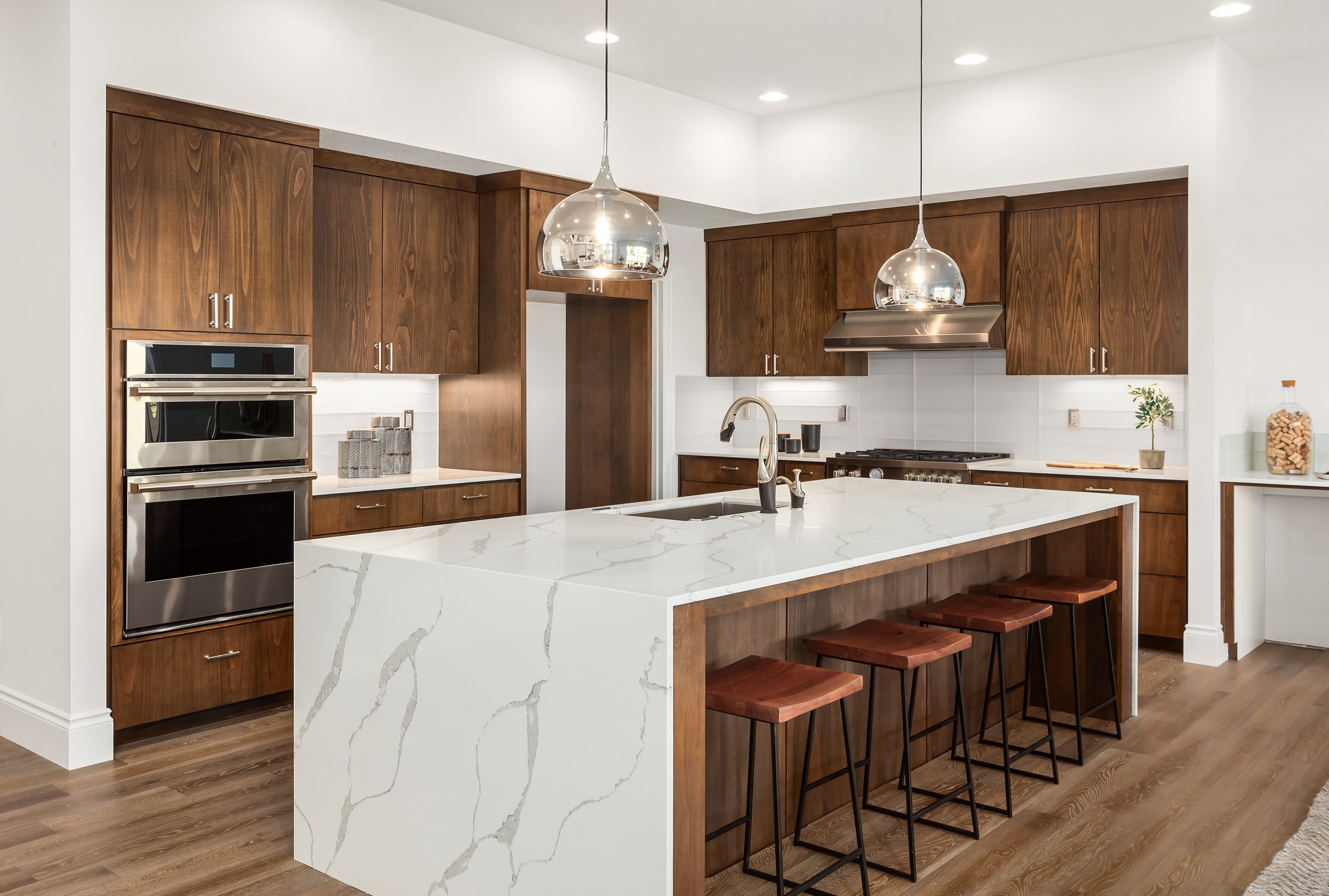 Modern kitchen with wood cabinets, marble island, pendant lights, and four barstools.