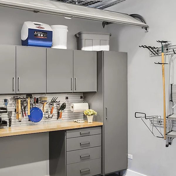 Gray garage cabinets, countertop, and hanging tools with storage bins and gardening supplies.