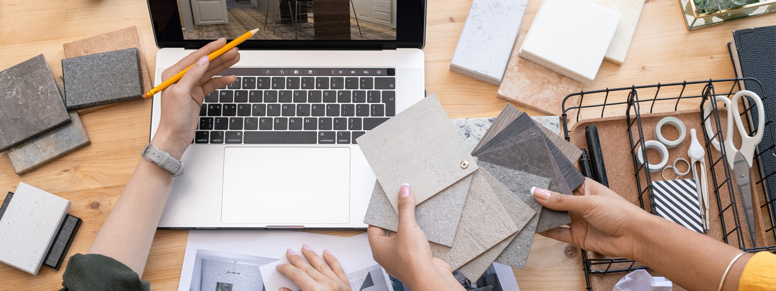 Two people select color samples near a laptop, surrounded by office and design supplies.