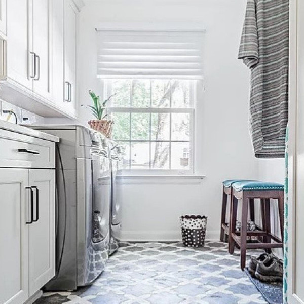 Bright laundry room with washer, dryer, cabinets, window, stools, and a basket on the floor.