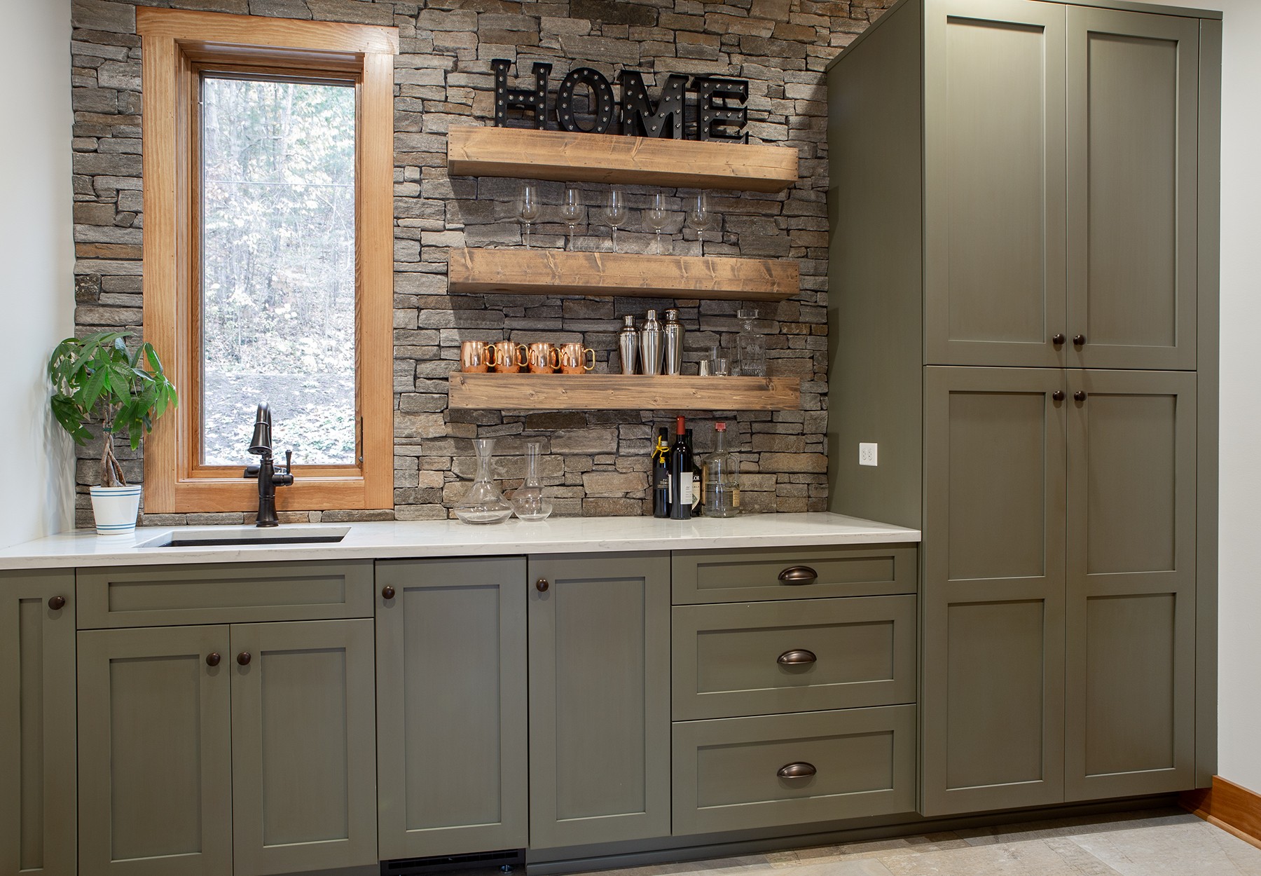 Modern kitchen with green cabinets, stone backsplash, open shelves, and a window over the sink.
