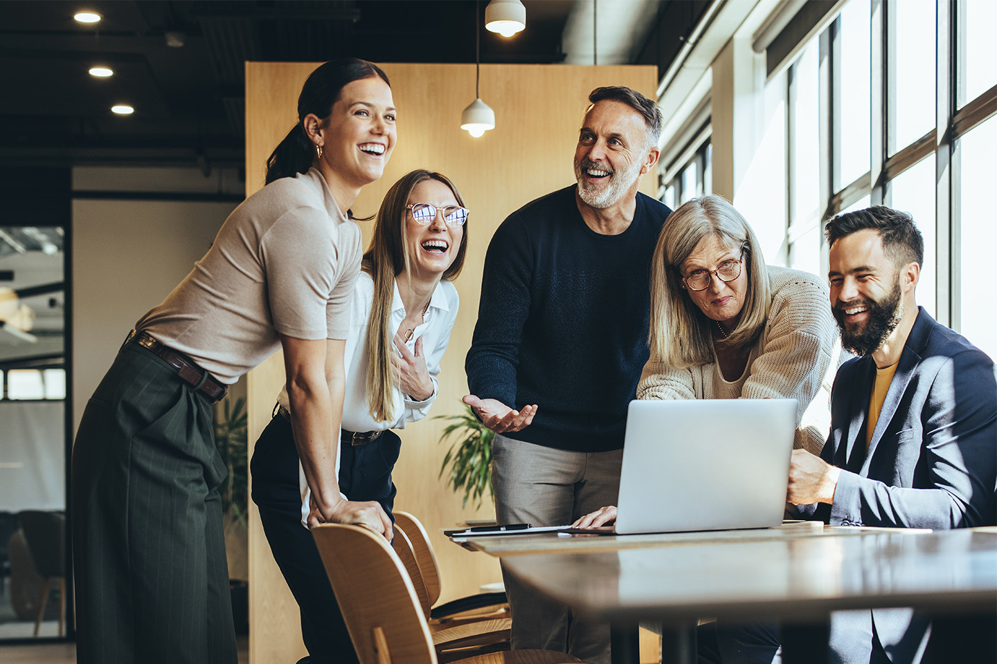 Five people looking at a computer and laughing.