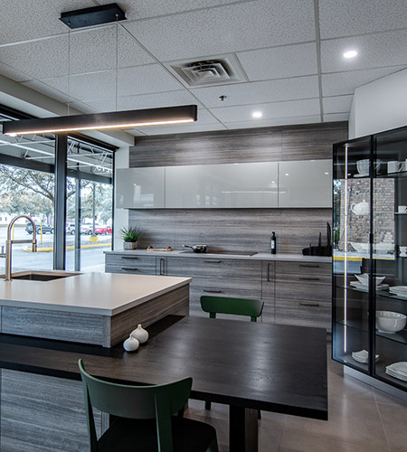 Modern kitchen with gray cabinets, island, dark table, green chairs, and glass display case.