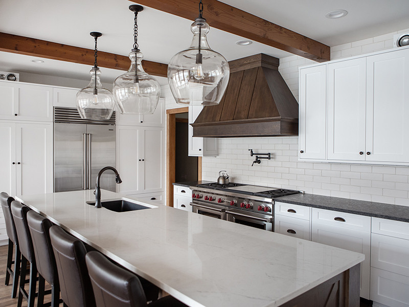 Modern kitchen with white cabinets, marble island, glass pendant lights, and dark wood accents.