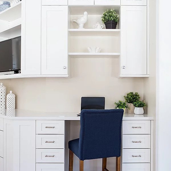 White home office nook with blue chair, laptop, green plants, and decorative shelves.
