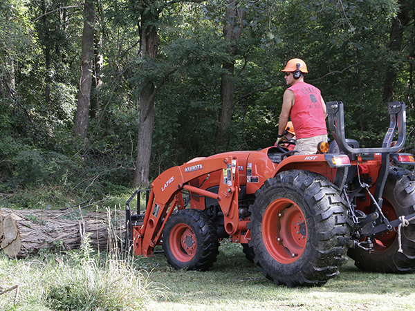 person driving an orange tractor moving large log