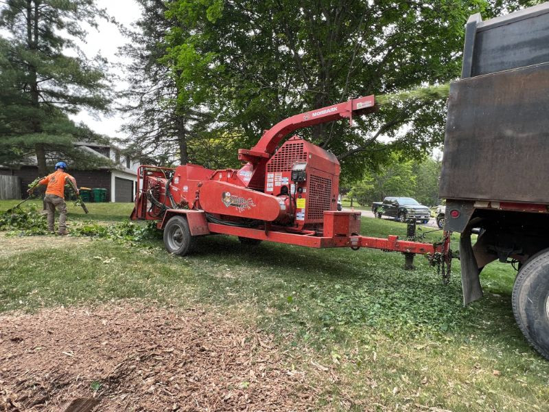 worker feeding branches into a wood chipper next to a truck