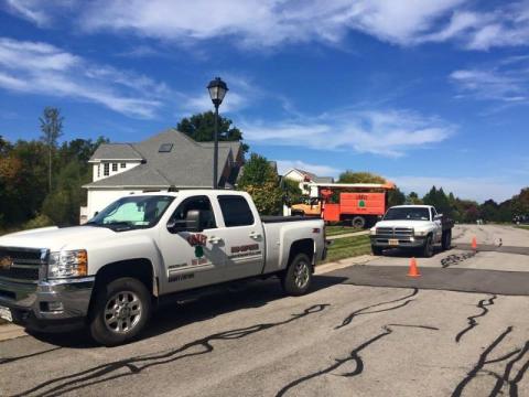 two utility trucks and safety cones parked on a suburban street