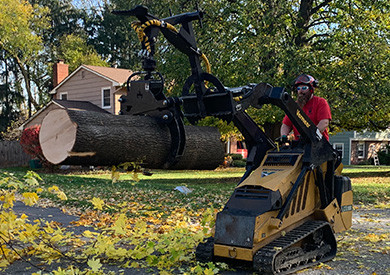 Man operating a small loader lifting a large tree log