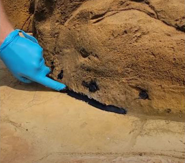 hand sealing silicone around faux rock waterfall for pool