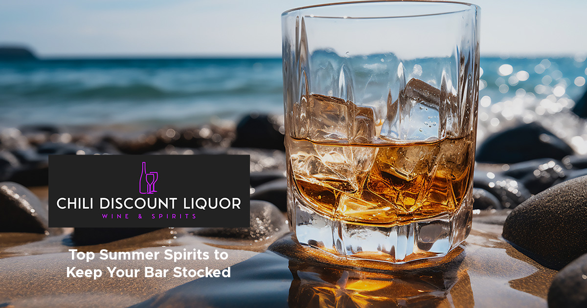 a glass of whiskey on sand by a body of water