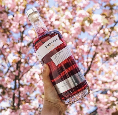 Hand holding a bottle of Empress 1908 gin against a background of cherry blossoms.
