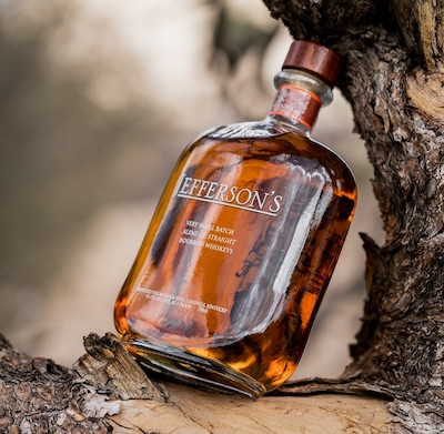 a bottle of Jefferson’s whiskey resting on a tree branch outdoors