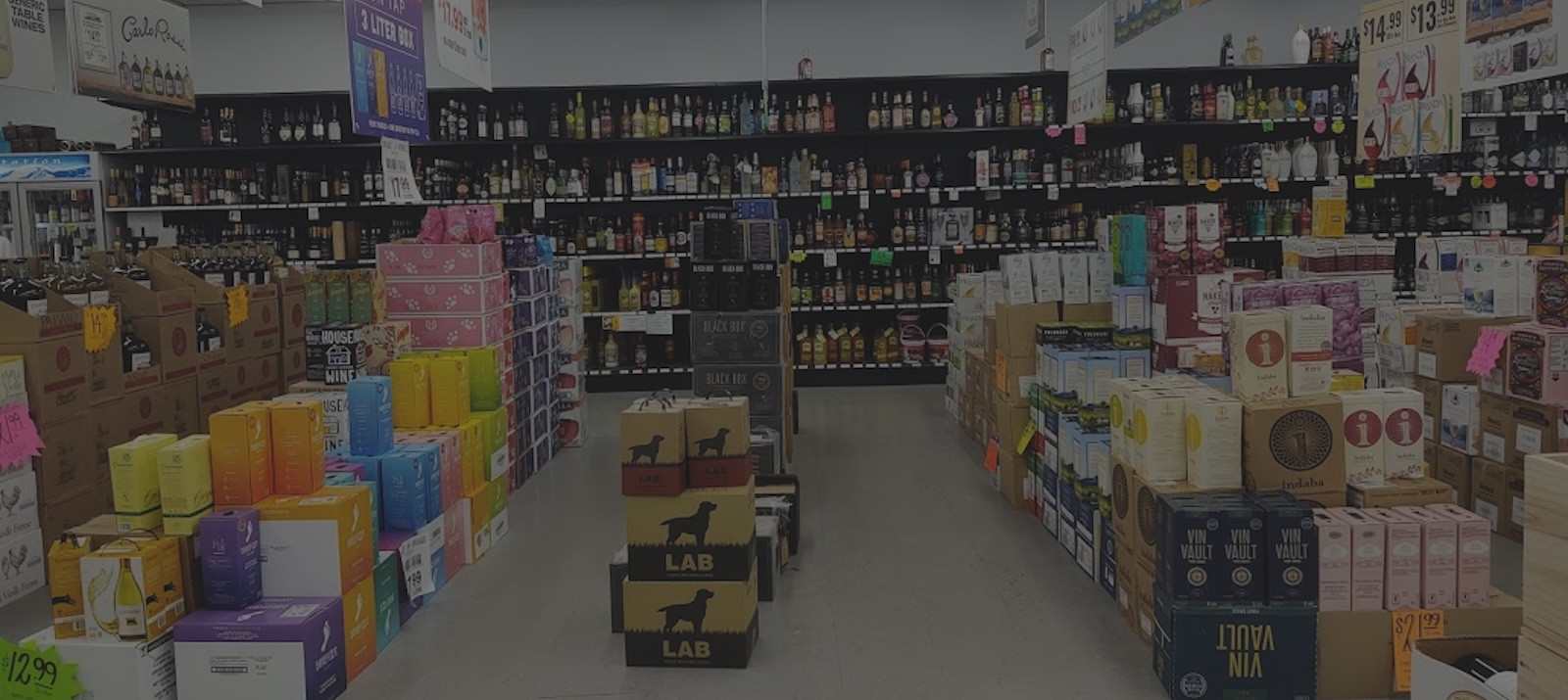 Liquor store interior with shelves and stacked boxes of various alcoholic beverages.