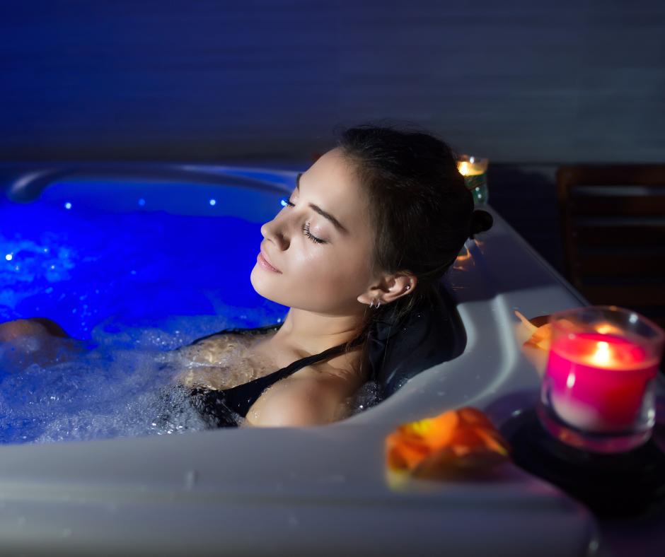 woman relaxing in hot tub with eyes closed and hot tub lights on, surrounded by candles and flower petals.