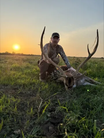 single hunter with axis buck trophy at sunset