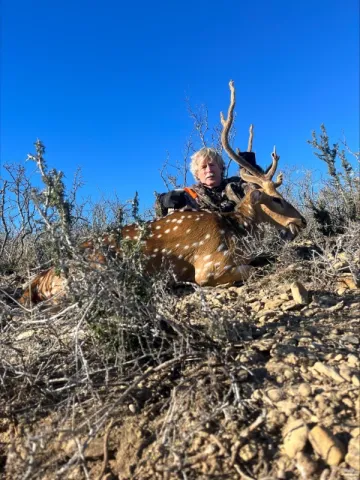 hunter with axis buck on a hill