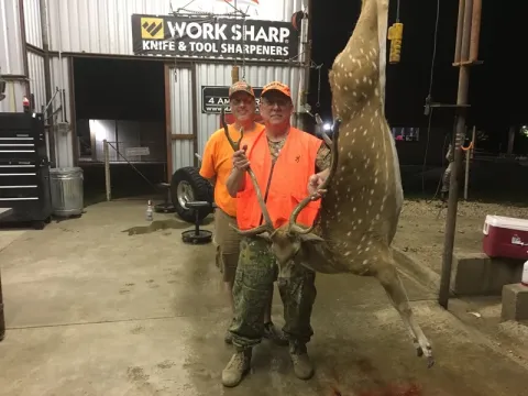 two hunters posing in garage with axis buck