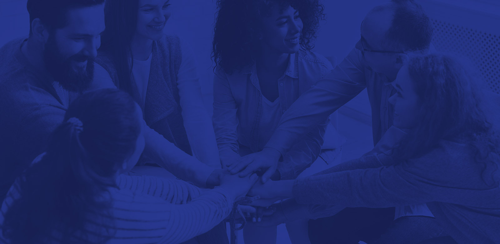 group of people sitting in a circle smiling and stacking hands in unity blue overlay