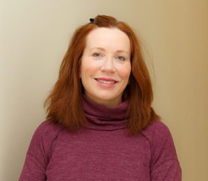 Dr. Elizabeth Arthur, wearing a purple turtleneck, smiling in front of a beige background.