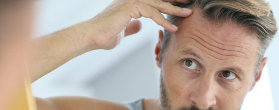 Man looking in mirror and examining his hairline with concern.