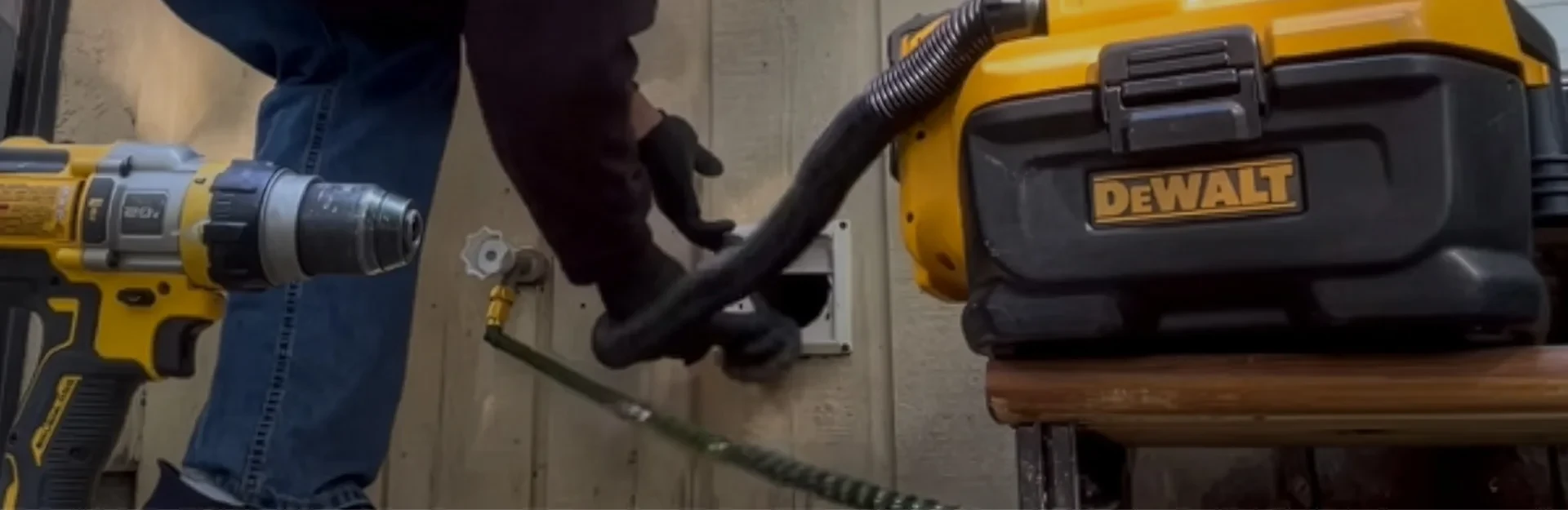Person using a drill and DeWalt vacuum to clean out a dryer vent on a wooden wall.