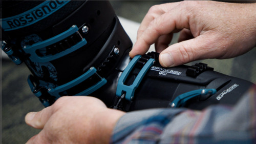 man in plaid shirt latches black and blue ski boot