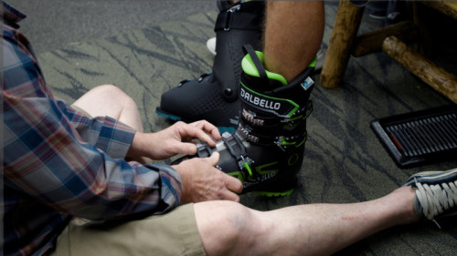 man in plaid shirt latching a green and black dabello ski boot