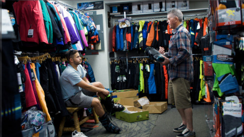 salesman speaking to man sitting down trying on ski boot