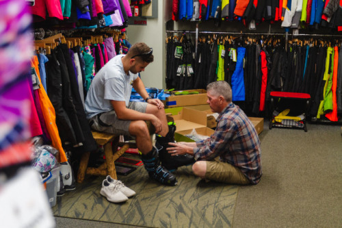 man sitting on floor helping customer trying on ski boots