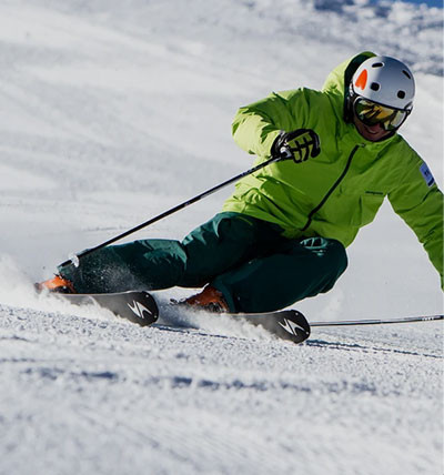 man in green jacket and snow pants skiing down a hill