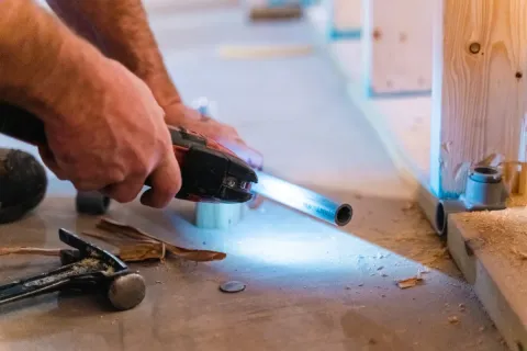 A person uses a power tool to cut a metal pipe on a construction site floor.