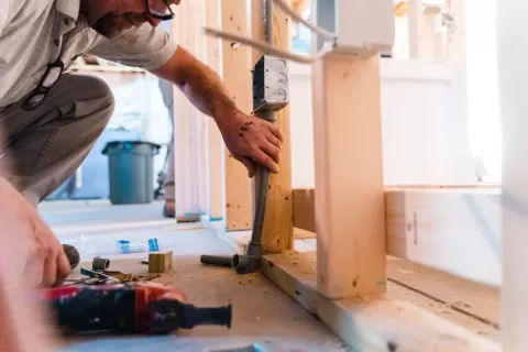 Person installing electrical outlet box on wooden framing during house construction.