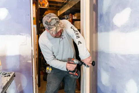 Person installing a doorknob with a drill in a room under construction or renovation.