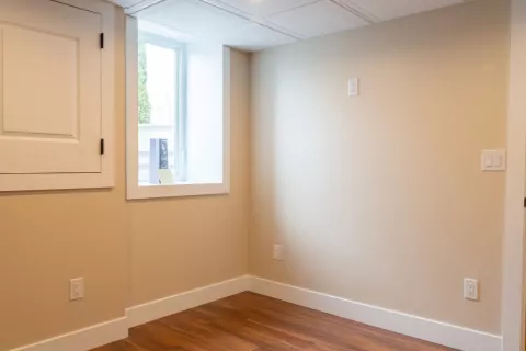 Small empty room with beige walls, wood flooring, a window, and a white door.