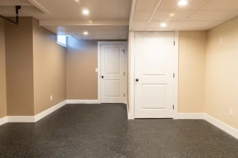 A finished basement room with beige walls, two white doors, and a small window.