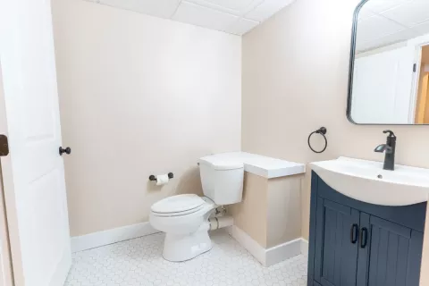 Minimalist bathroom with a toilet, small vanity, mirror, and white hexagon tile floor.