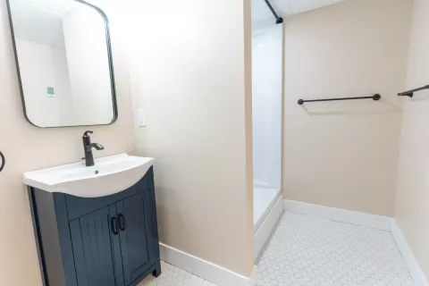 Small bathroom with a dark vanity, mirror, walk-in shower, and hexagonal tile floor.
