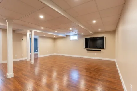 Spacious finished basement with wood flooring, beige walls, and a wall-mounted TV.