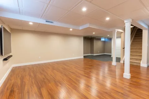 Spacious finished basement with hardwood floors, beige walls, and stairs leading upstairs.