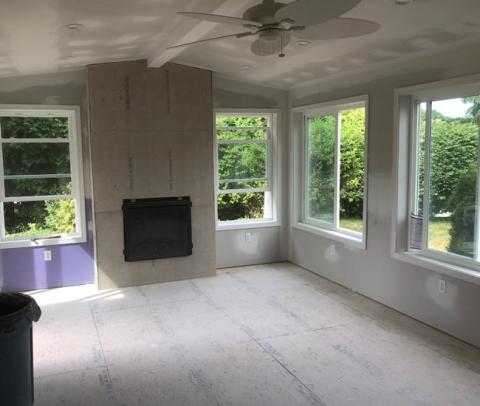A bright, unfinished room with large windows and a fireplace under construction.