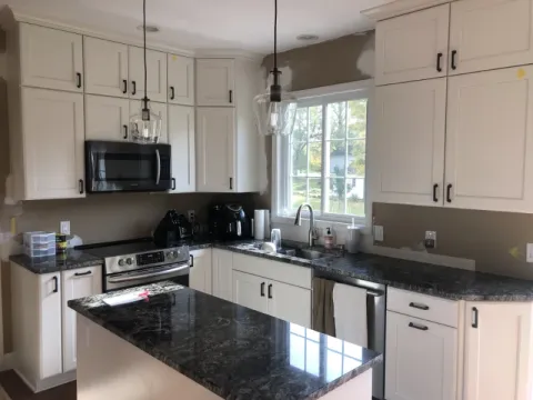 Modern kitchen with white cabinets, dark countertops, a stove, microwave, and a window.