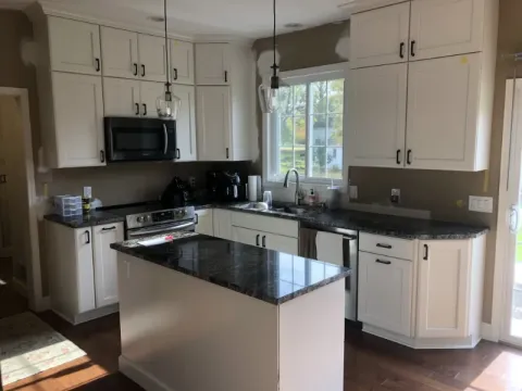Modern kitchen with white cabinets, black countertops, island, and stainless steel appliances.
