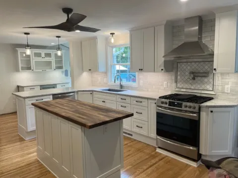 Modern kitchen with white cabinets, wood island, stainless steel appliances, and tile backsplash.