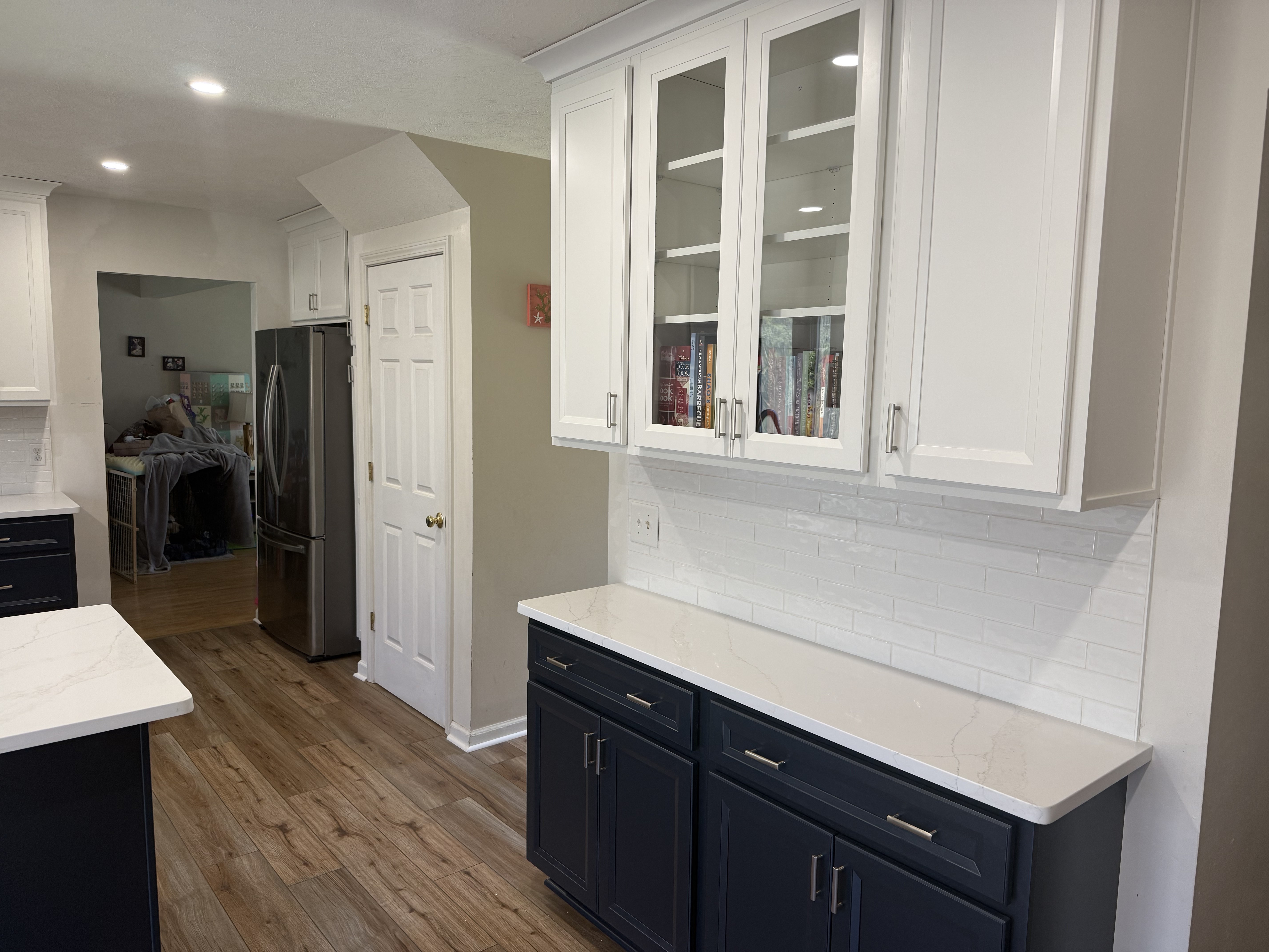 Modern kitchen with white upper cabinets, dark blue lower cabinets, and wood flooring.