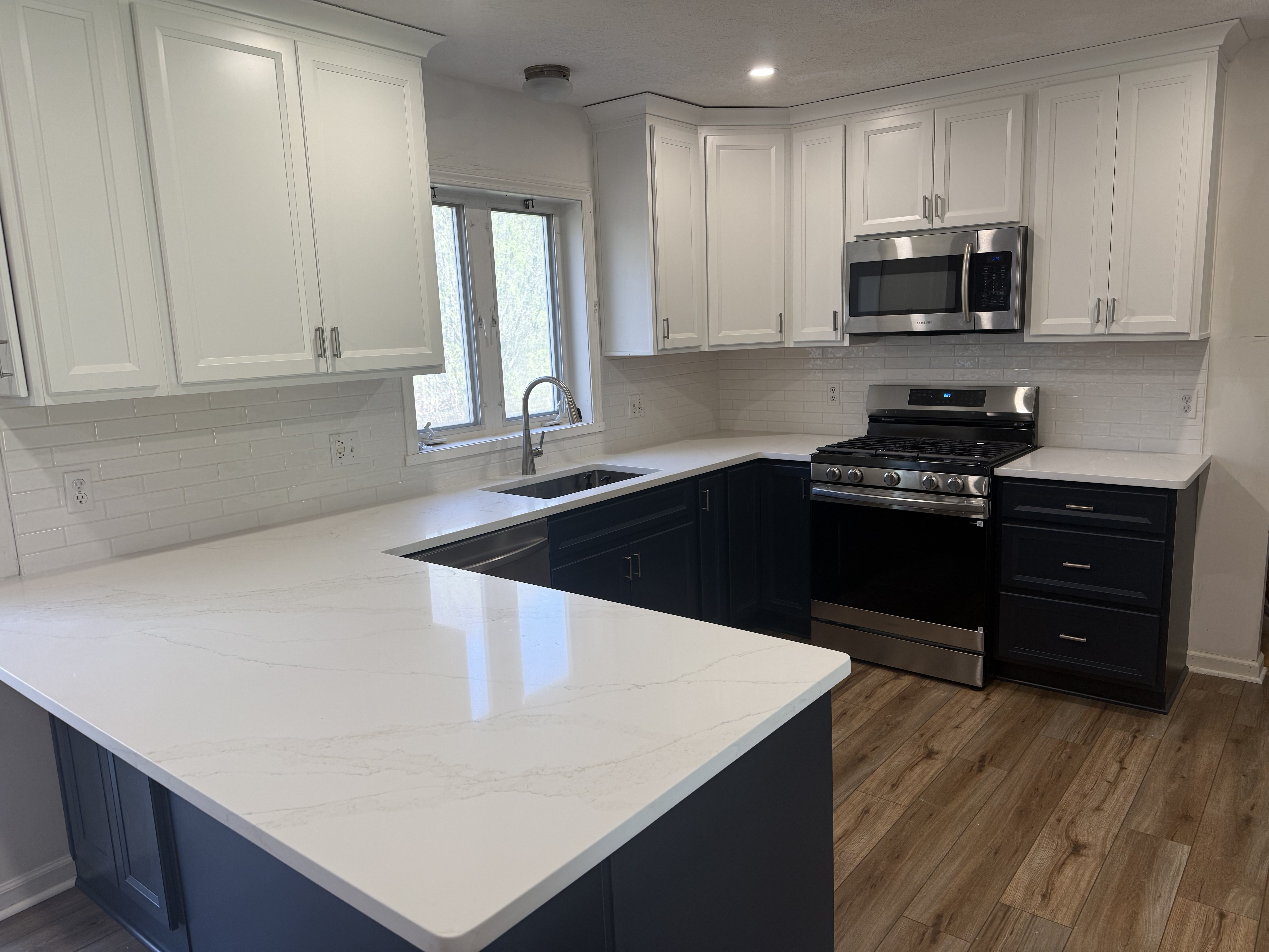 Modern kitchen with white cabinets, marble counters, stainless appliances, and wood flooring.