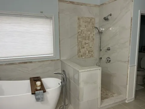 A refinished white bathroom with a new shower stall and bathtub.