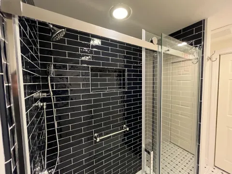 A refinished bathroom with black subway tiles on the walls.