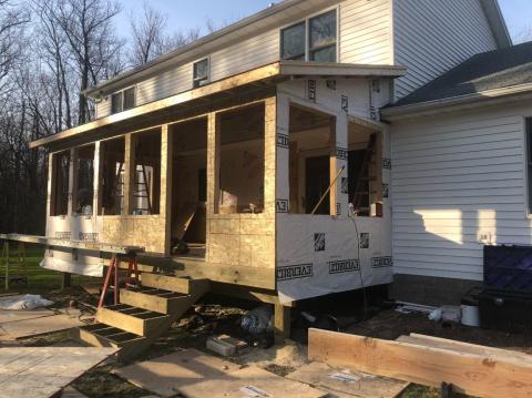 A house with a partially built wooden porch addition under construction in daylight.
